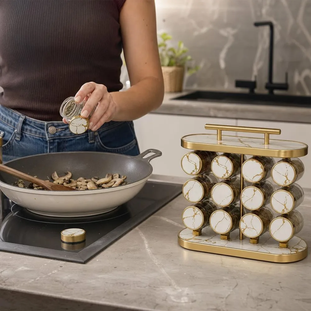 1) El especiero sobre el mesón de una cocina pequeña mientras alguien lo gira para tomar un frasco. 2) Primer plano de una tapa tipo mármol con el detalle dorado y el vidrio mostrando la especia.